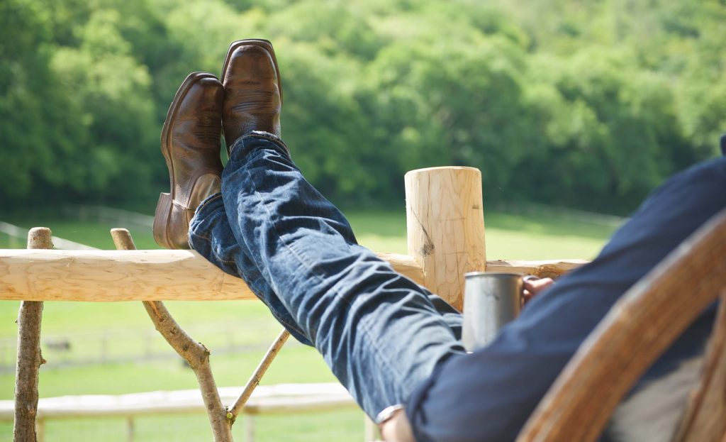 A guest sitting on the porch of his cabin at Loose Reins with his feet up looking out over the woodland view
