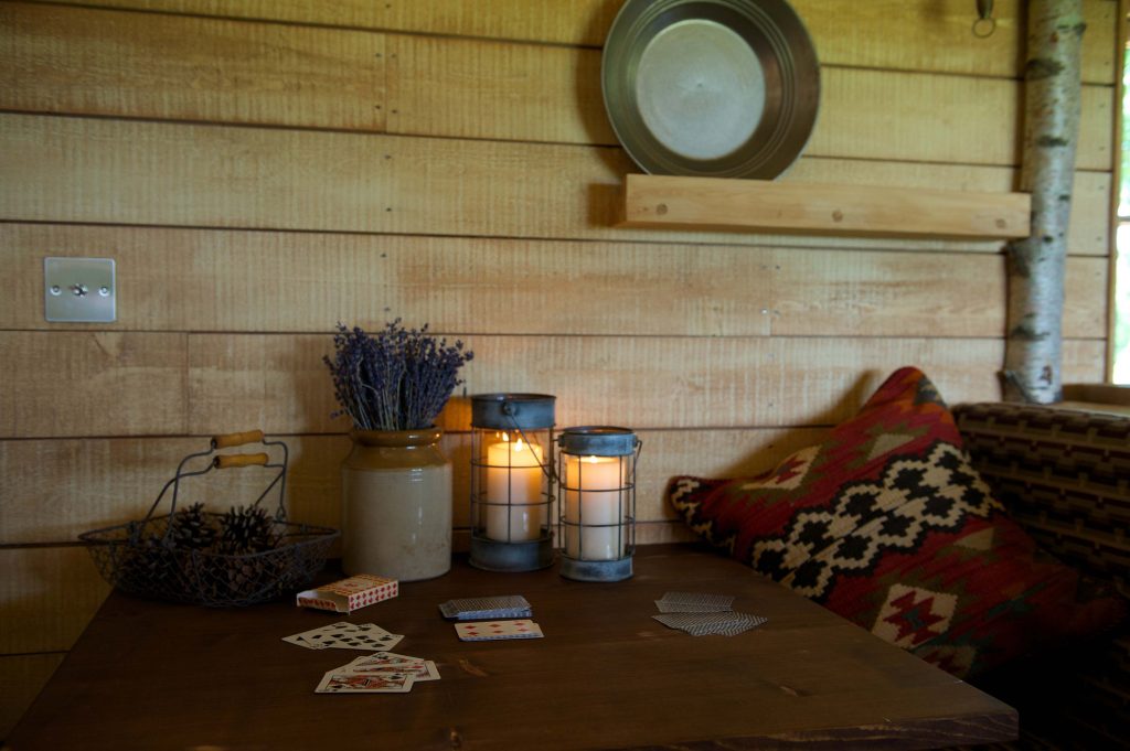A game of cards on the table inside the Cabin at Loose Reins with lit candles and cosy cushions
