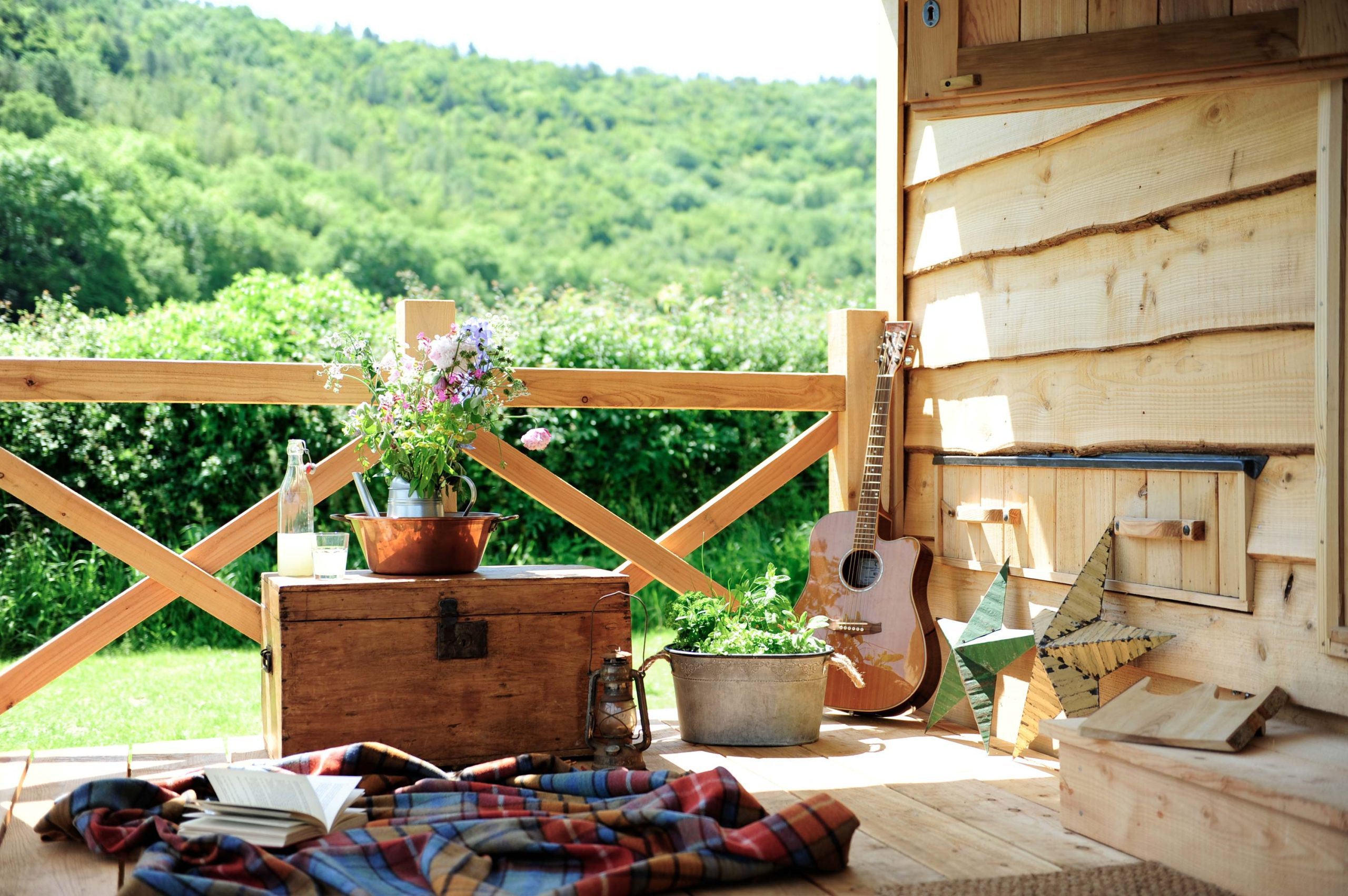 A blanket on the floor of the cabin porch at Loose Reins with a guitar fresh flowers and a herb planter