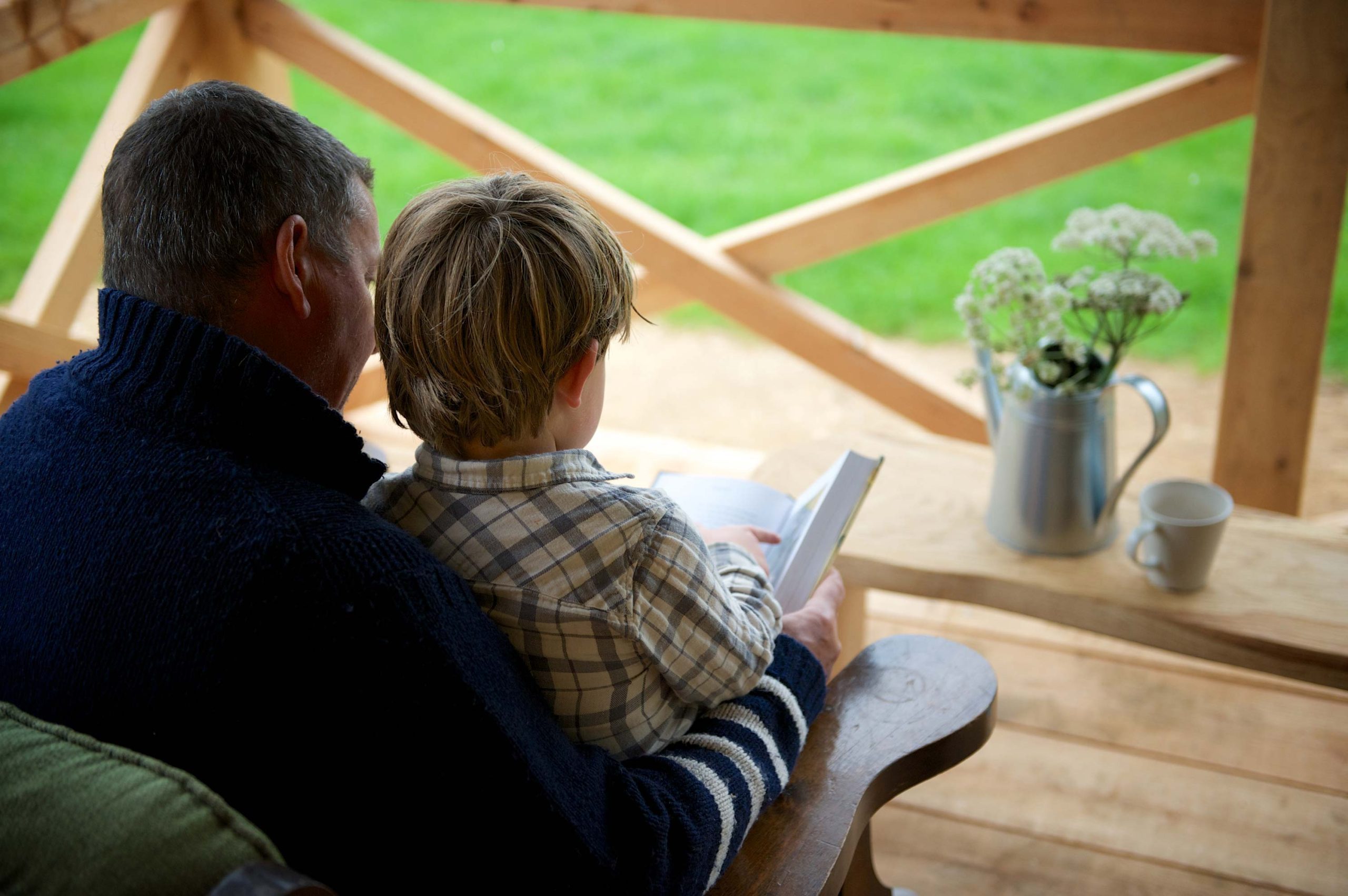 A man and his son reading a story book on the porch of a cabin at Loose Reins