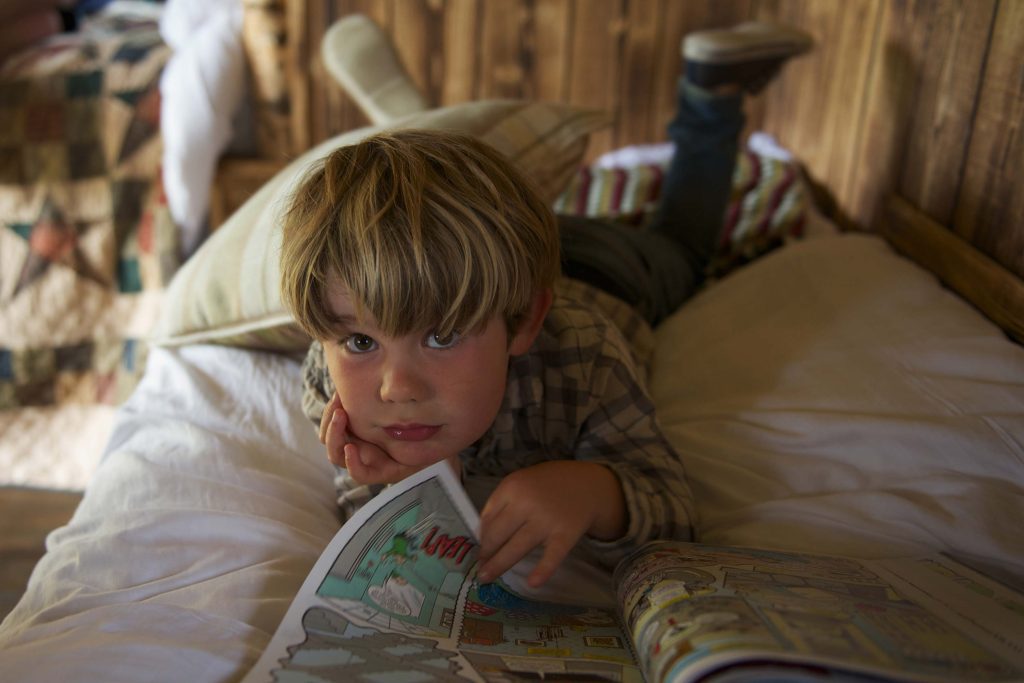 A young boy reading a comic and lying on one of the beds inside the Cabin at Loose Reins