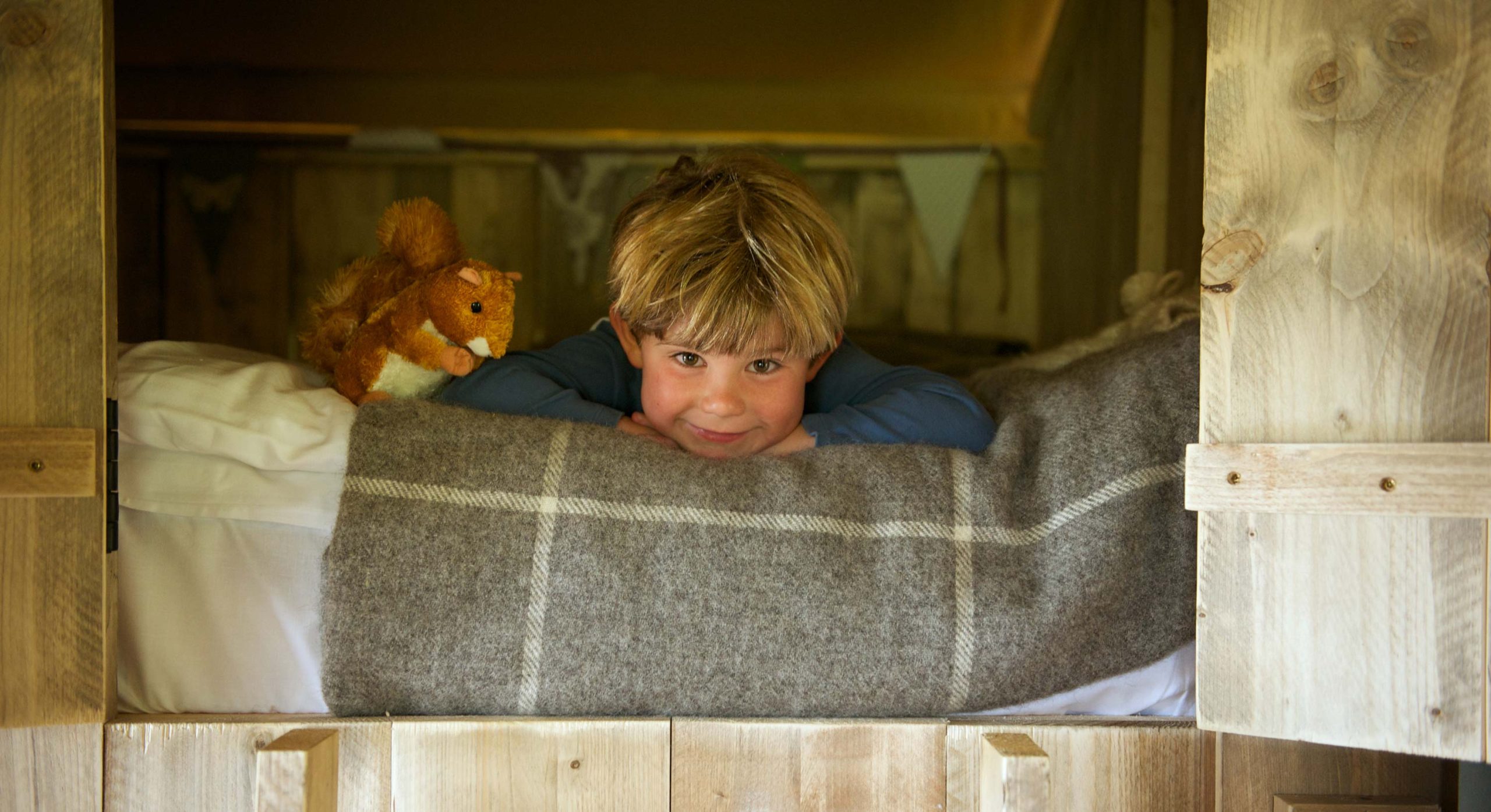 A young boy lying on the cabin bed with a soft toy inside a lodge at Loose Reins