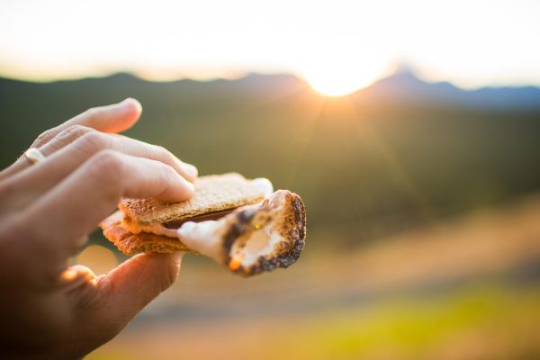 Close-up shot of a person roasting marshmallow enjoying s'more by a campfire