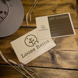 A gift Voucher for Loose Reins Glamping set on a rustic wooden table