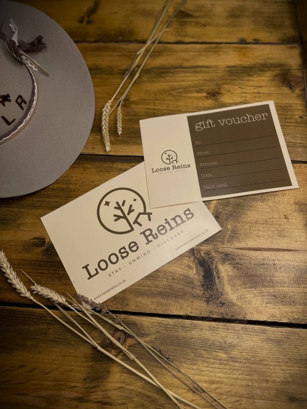 A gift Voucher for Loose Reins Glamping set on a rustic wooden table